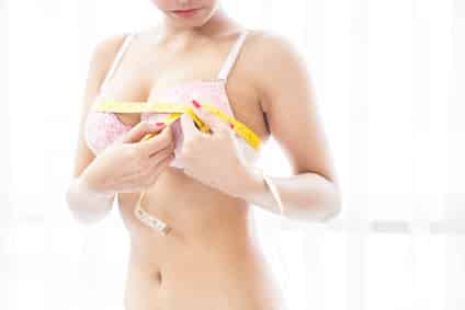 Woman measuring breast size with a yellow tape on room.